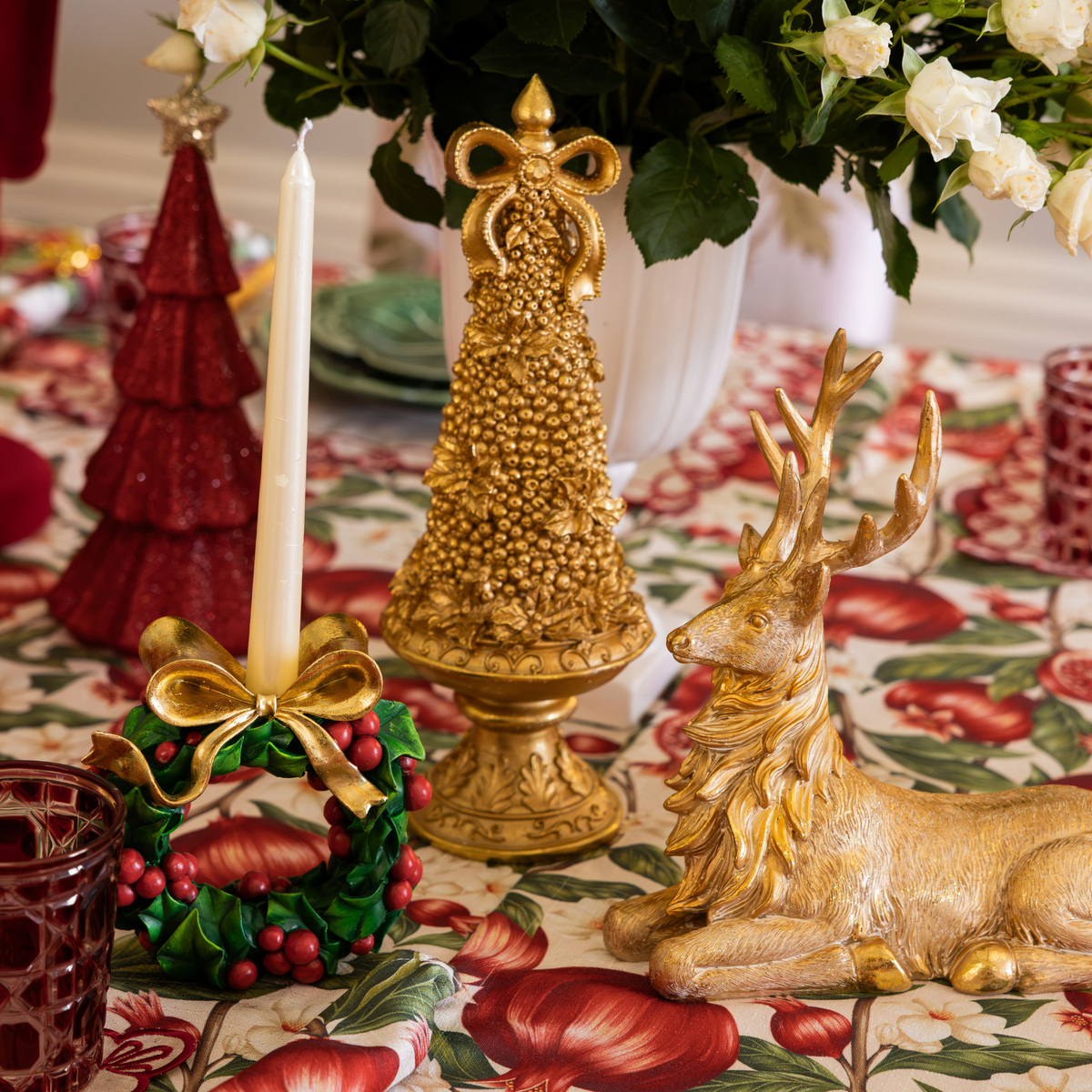 Pomegranate Christmas table styled with gold Christmas tree, holly wreath candle holders and gold resting reindeer