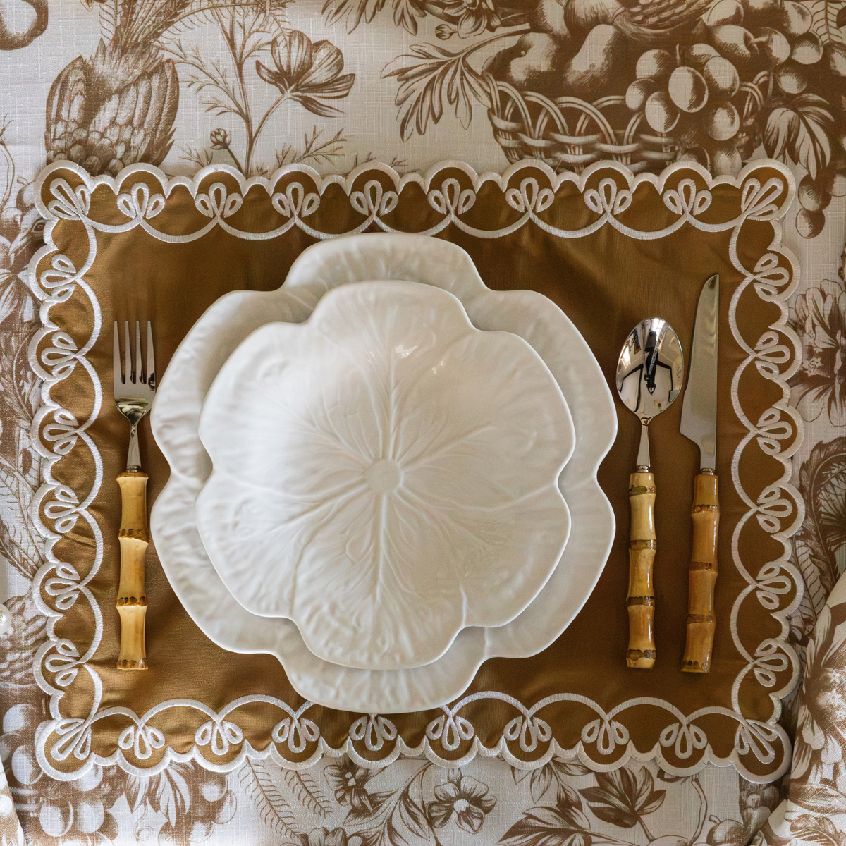 Gold Toile Christmas table styled with gold placemats with ivory embroidery and white cabbage plates